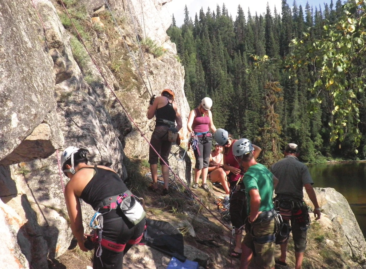 A top roping group at a lakeside crag, with participants gathered at the base while two climbers work on adjacent routes