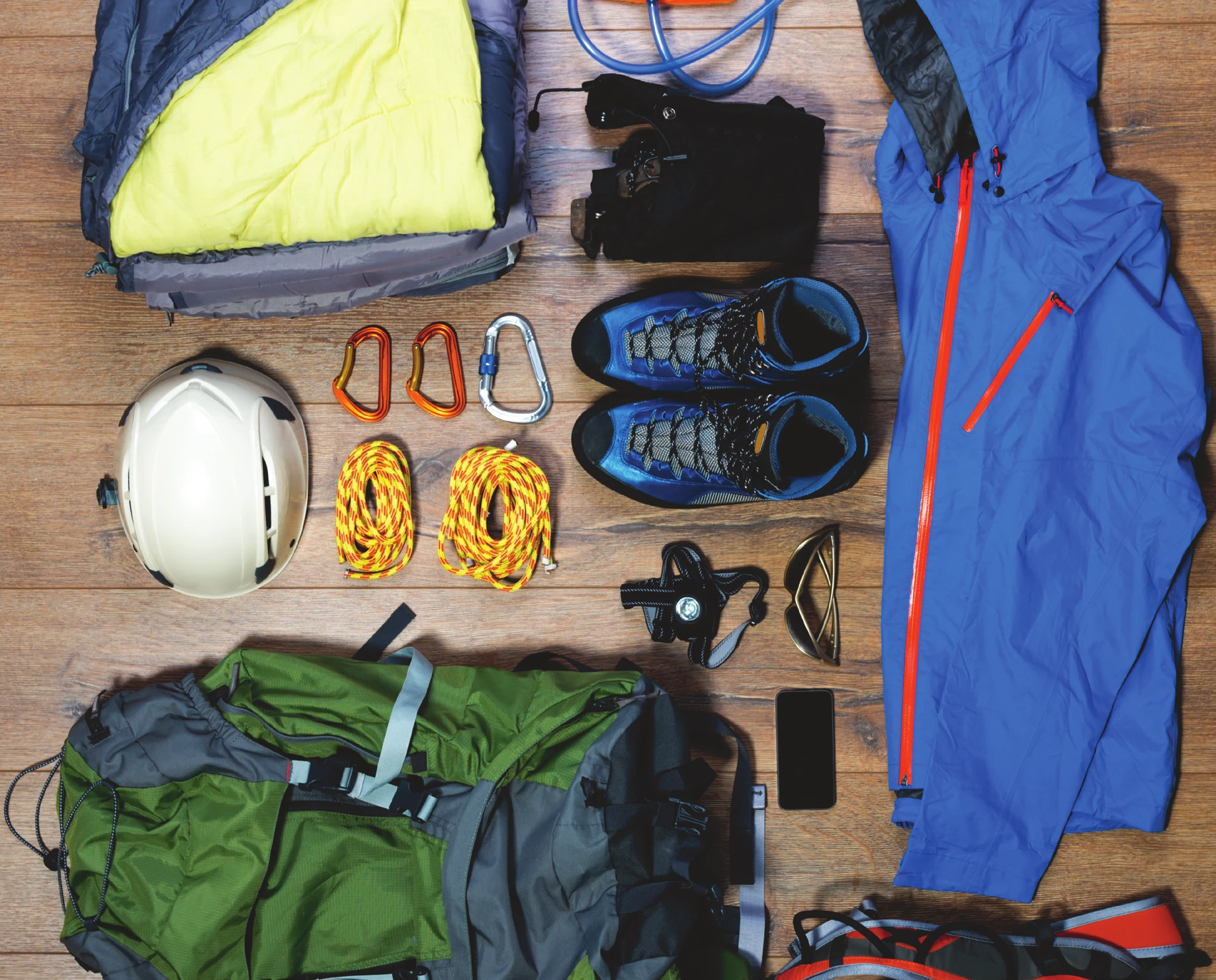 Personal climbing equipment laid out — helmet, carabiners, cord, approach shoes, harness, sunglasses, shell jacket and pants, phone, and packs
