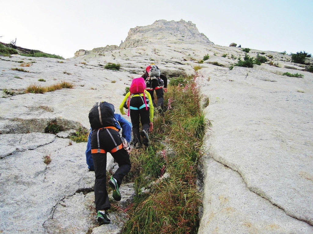 A group moving up a low-angle granite slab on approach to a climbing venue