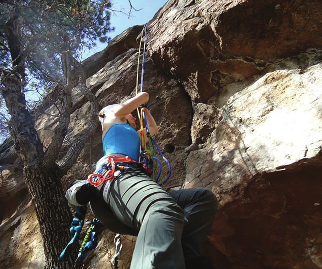 A climber ascending a fixed rope on prusiks at the base of a crag