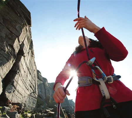 Un participant faisant coulisser la corde dans un descendeur au pied d’une falaise, à contre-jour