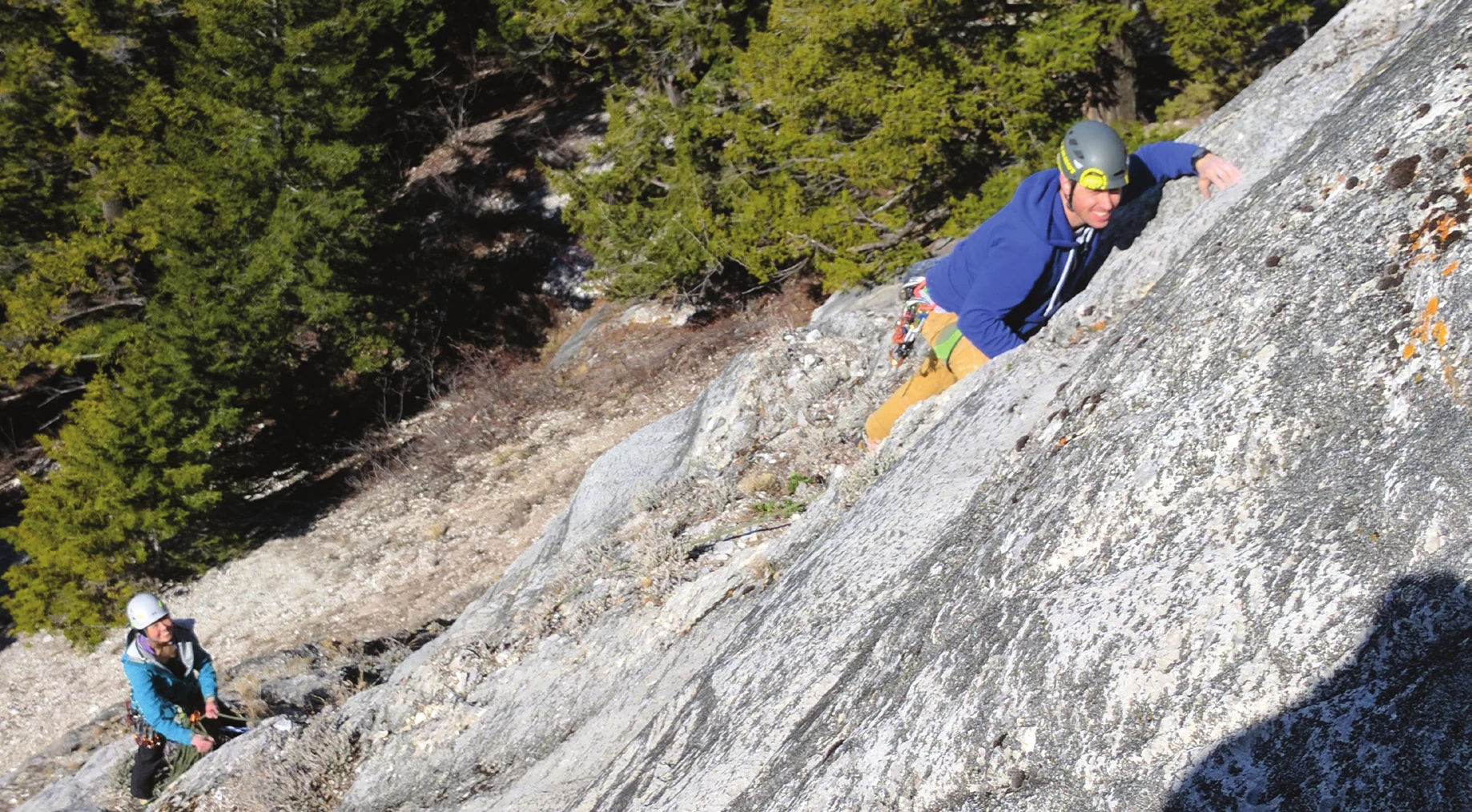 Un grimpeur progressant sur une dalle peu inclinée en moulinette, l’assureur visible en contrebas