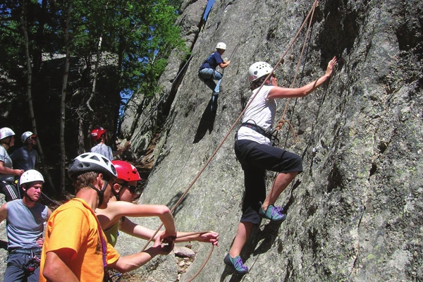 Un groupe d’escalade en moulinette au pied d’une falaise, un instructeur encadrant un assureur pendant qu’un grimpeur progresse dans la voie