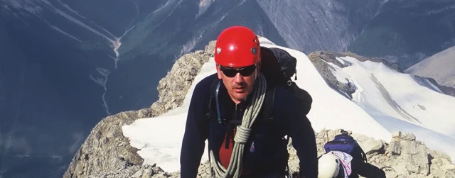 Un grimpeur portant un casque d’escalade rouge sur une arête enneigée
